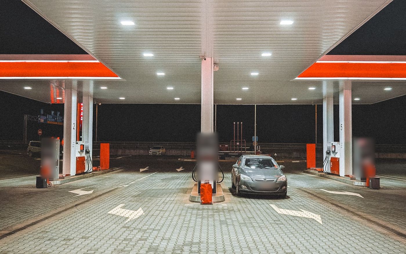 A modern forecourt at night with a single car at the pumps under a lit canopy