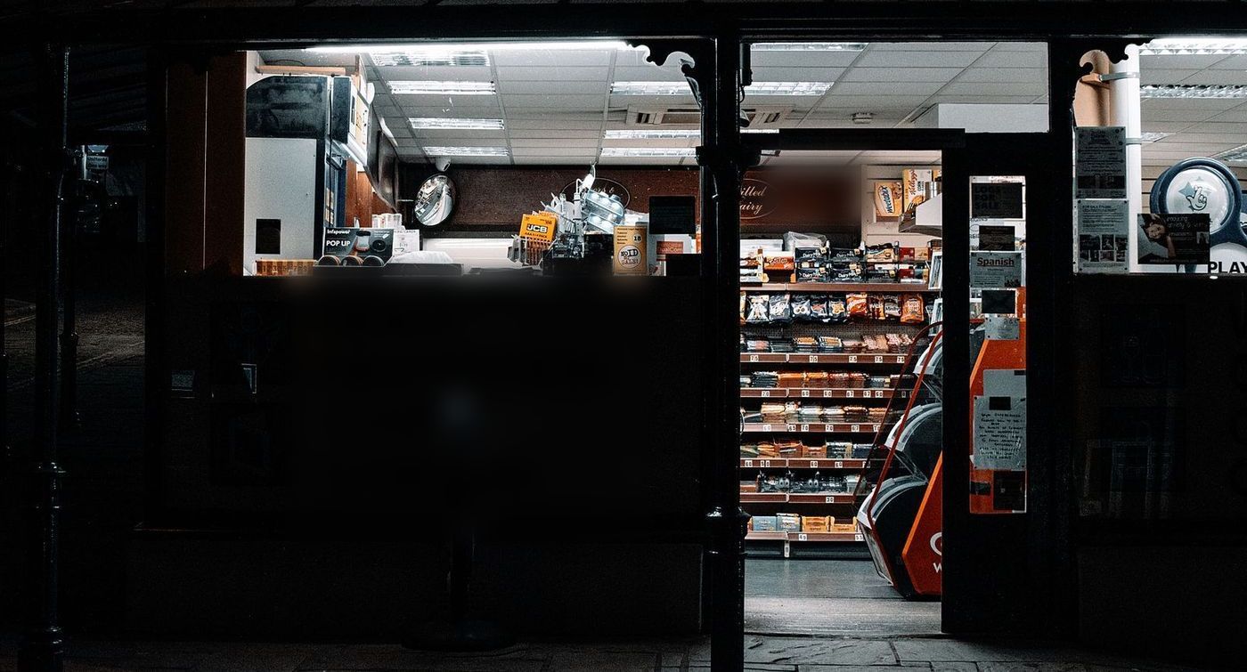 A forecourt convenience store glowing at night, shelves of snacks visible through the door