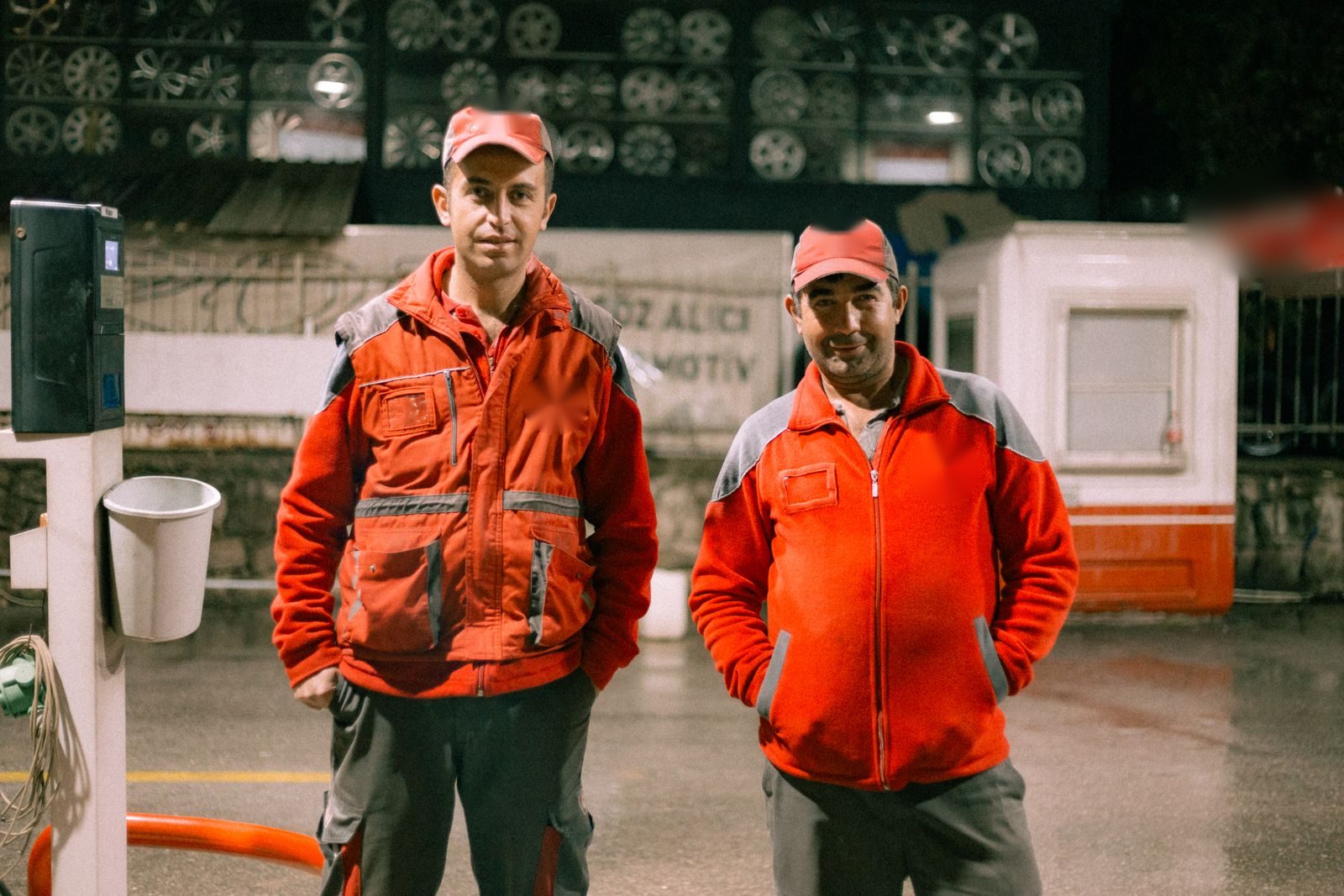 Two smiling forecourt attendants in red uniforms on shift at night